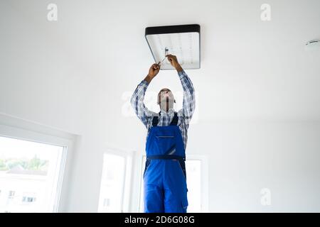 African Maintenance Electrician On Ladder Fixing And Installing Light Stock Photo