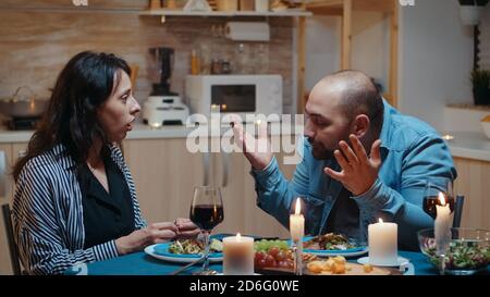 Angry man for positive pragnancy test during romantic dinner. Woman surprising her husband being pregnant, unhappy, nervous, partner, unwanted baby, frustrated for results. Stock Photo