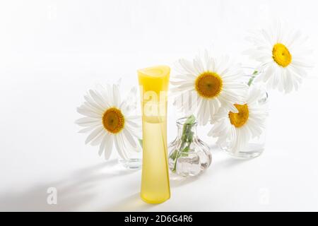 Beautiful chamomiles or daisy flowers and cosmetic product in bottle on white. Floral composition with perfume or essential oils. Organic cosmetology, Stock Photo