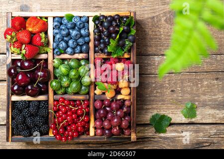 Mix of fresh berries with leaves in wooden box on rustic background. Forest summer berries. Various berries healthy food. Top view. Flat lay Stock Photo