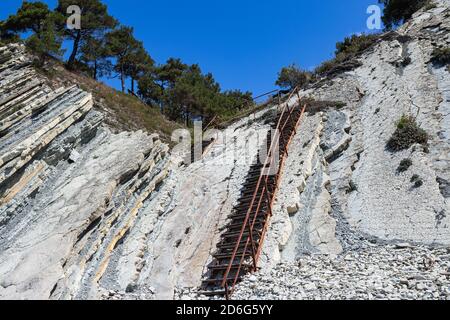 An old metal staircase and massive white rocks on a wild beach. The path to the campsite goes through the forest. Summer landscape on a clear day Stock Photo