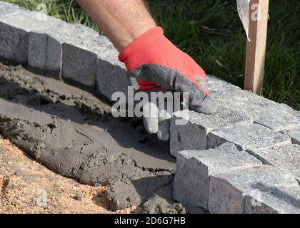 Hands in gloves of a builder worker laying on the granite cobblestone sett  on sand and mortar , paving  sidewalk Stock Photo