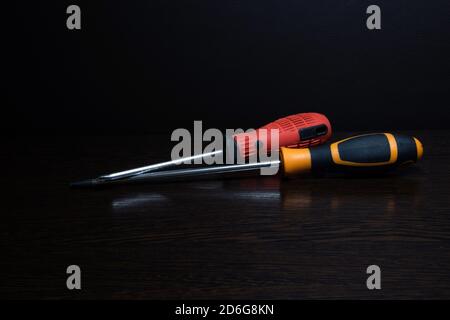 Two screwdrivers of different colors with reflection lying on a dark wooden surface Stock Photo