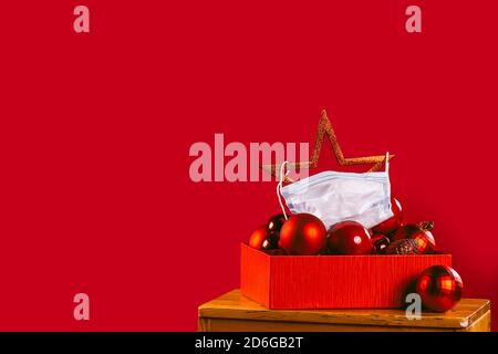 Christmas star with medical mask in a box with red Xmas decorations. New normal. Holidays in pandemic on red background Stock Photo