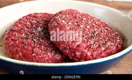 Two raw hamburger patties that are unseasoned, sitting outside in order to reach room temperature before putting them on the grill. Stock Photo
