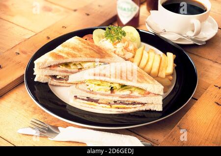 Sandwich with ham, cheese, tomatoes, lettuce, toasted bread, french fries and a cup of coffee Stock Photo