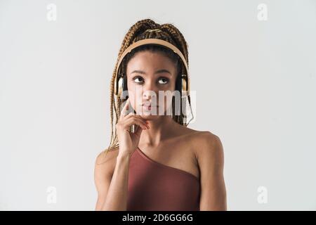 Portrait of beautiful pensive african brunette woman with dreadlocks a listening music via wireless headphones isolated on white background Stock Photo