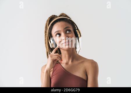 Portrait of beautiful smiling african brunette woman with dreadlocks a listening music via wireless headphones isolated on white background, looking a Stock Photo