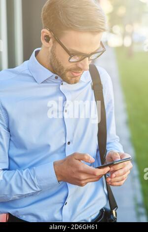 Making important call. Young handsome businessman wearing wireless earphones using smartphone while standing outdoors Stock Photo