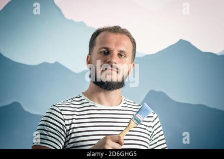 Bearded man painter holding paint brush in front of the wall. how to make repairs yourself Stock Photo