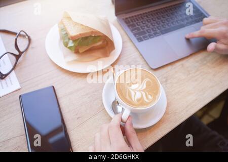Top view of a freelancer or businessman using laptop, drinking coffee and having breakfast while working remotely in cafe Stock Photo