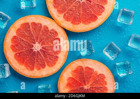 slices of orange grapefruit and lemon on a blue background, with ice around it and drops of water Stock Photo