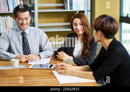 three asian businesspeople man and woman sitting at desk discussing business proposal in office Stock Photo