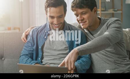 Adorable Male Gay Couple Spend Time at Home. They Sit on a Sofa and Use the Laptop. They Browse Online. Partner Puts His Hand Around His Lover. Room Stock Photo