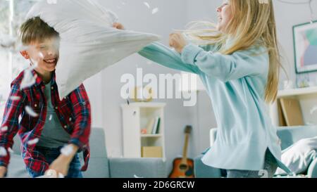 Adorable Little Boy and Sweet Little Girl Have a Pillow Fight in the Sunny Living Room. Siblings Having Fun Fighting with Pillows, Feathers Flying Stock Photo