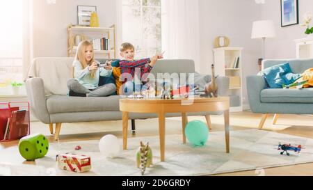 At Home: Cute Girl Playing in Video Game Console, Using Joystick Controller, Her Younger Brothe Cheers for Her. Happy Children Playing Videogames. Stock Photo