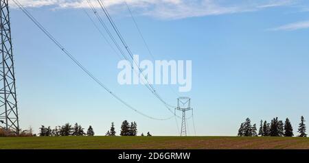 Tall steel power cable pylons supporting electricity cables over flat ground, some trees in distance Stock Photo