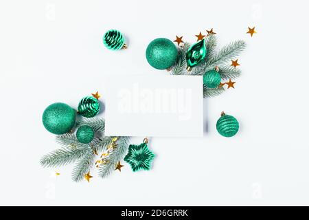 Christmas composition with blank paper sheet postcard, fir branches and green baubles on white background. Stock Photo
