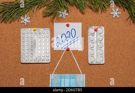 Medical mask, white pills, white sticky note with 2020 pinned on notice board which is decorated with pine twigs and snowflakes. Healthcare, christmas Stock Photo
