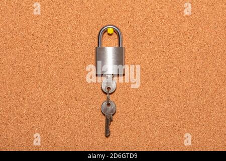 Closed padlock with keys hanging from it on an empty corkwood notice board in business office. Safety and security reminder, business closure, busines Stock Photo
