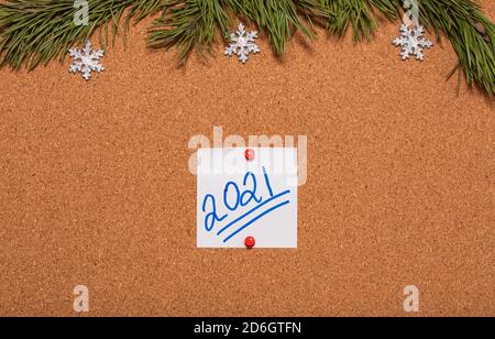 White sticky note with 2021 handwritten on it pinned on notice board which is decorated with pine twigs and snowflakes. 2021 Christmas, new years cele Stock Photo