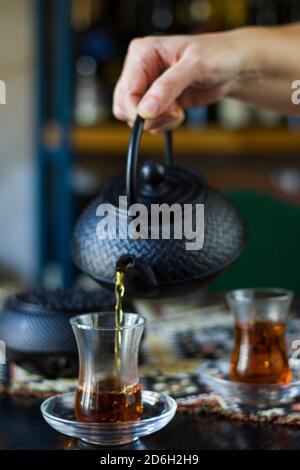 Black tea and teapot in hand, Turkish tea glasses and old iron teapot Stock Photo