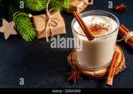Christmas Hot Drink. Eggnog with Cinnamon in Glass with Branches Fir Tree on Dark Background. Stock Photo