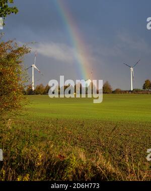 a big rainbow over a field on which wind turbines stand Stock Photo
