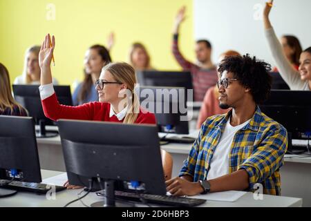 Students raising hands for an answer on professor question at an informatics lecture in the university computer classroom. Smart young people study at Stock Photo