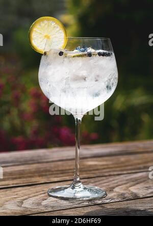 Gin and tonic cocktail drink outside on a wooden table with ice, lemon and lime Stock Photo