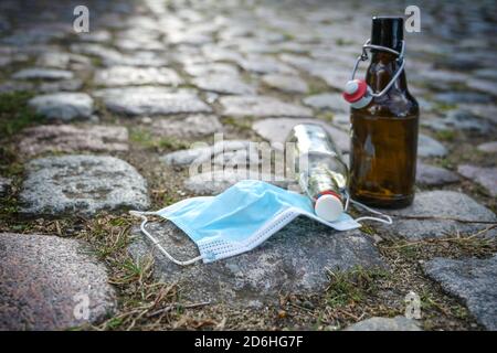 Beer and liquor bottles and a surgical face mask left on a cobblestone road, while bars have closed due to infection with coronavirus and covid-19, so Stock Photo