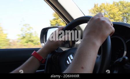 Odessa, Ukraine - 09 06 2020: Closeup of young man hands on steering wheel while speed driving a car. Blur view of autumn yellow trees outside auto wi Stock Photo