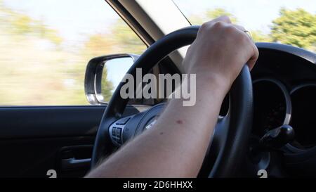 Closeup of young man hand on steering wheel while speed driving a car. Blur view of autumn yellow trees outside the side window and windshield Stock Photo