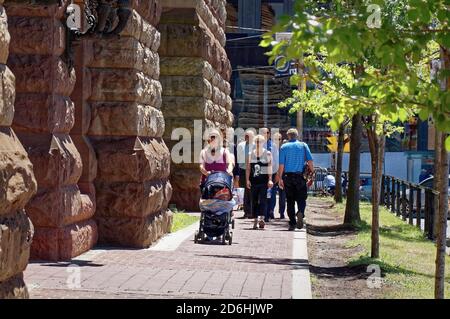 TORONTO, CANADA - 06 27 2016: People stroding along the sidewalk with green young trees beside the stony wall of Toronto Old City Hall on a sunny Stock Photo