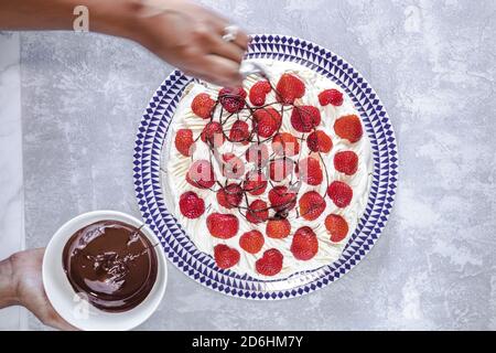 Chocolate being drizzled on a pavlova topped with strawberries Stock Photo