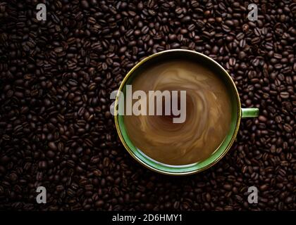 Green Mug of Coffee Swirling with Milk Sitting on Coffee Beans Stock Photo