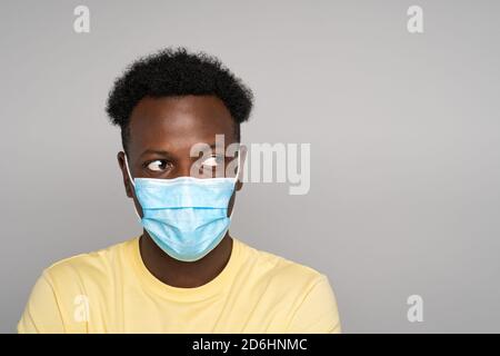 Serious Afro-American man in yellow t-shirt wear face mask looking away at copy space for advertising, offering, product, promotion text, sale, over s Stock Photo