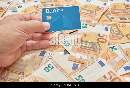 A white or Caucasian man holds in his hand a microchipped credit or debit card on a background of fifty euro bills Stock Photo