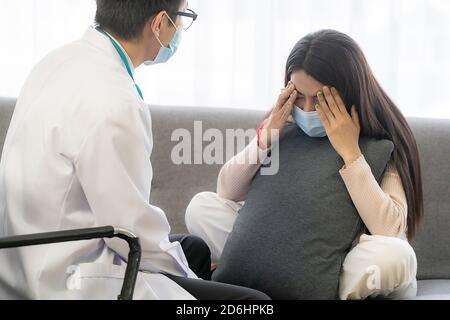 Portait of asian female patient with face mask talking to Psychotherapist doctor for consult about her mental health after stress strain from quaranti Stock Photo