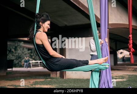 Young caucasian woman winding up whilst using her stretch fabric as a hammock hanging on a bridge. Stock Photo