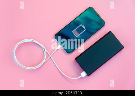 Smartphone charging with power bank on pink background. Flat lay Stock Photo