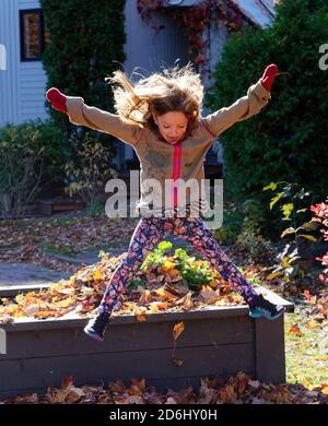 A six year old girl doing a star jump into a pile of autumn leaves Stock Photo