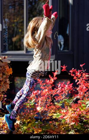 A six year old girl doing a star jump into a ple of autumn leaves Stock Photo
