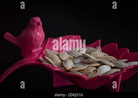 Pumpkin seeds in bird and leaf shaped pink bowl Stock Photo
