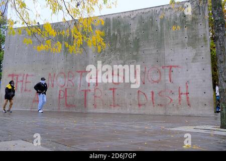 Manchester Piccadilly Gardens wall painted with lockdown protest graffiti THE NORTH IS NOT A PETRI DISH. Men in masks walk by it. Stock Photo