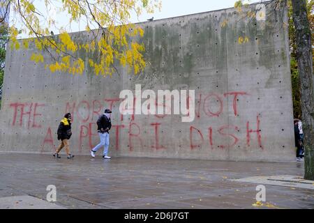 Manchester Piccadilly Gardens wall painted with lockdown protest graffiti THE NORTH IS NOT A PETRI DISH. Woman in mask walk by it. Stock Photo