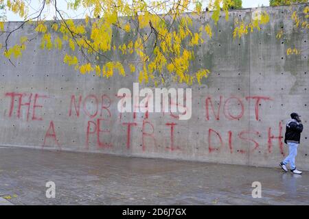 Manchester Piccadilly Gardens wall painted with lockdown protest graffiti THE NORTH IS NOT A PETRI DISH. Man walk by it. Stock Photo