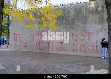 Manchester Piccadilly Gardens wall painted with lockdown protest graffiti THE NORTH IS NOT A PETRI DISH. Woman in mask walk by it. Stock Photo