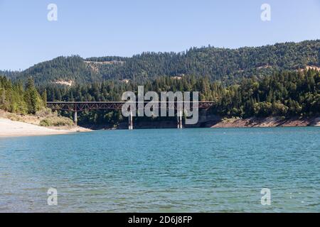 Looking across the surface of Lost Creek Lake to a side view of Peyton Bridge and Highway 62 with thick trees covering the Cascade Mountains near Pros Stock Photo