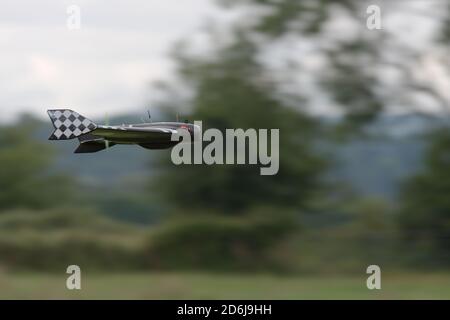 Pan shot technique creates a blurred background as this remote control delta FPV drone flies pas at high speed. Rural background and racing pattern. Stock Photo